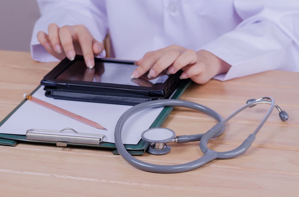 Occupational health clinician reviewing records on a tablet beside a stethoscope — biological monitoring follow-up