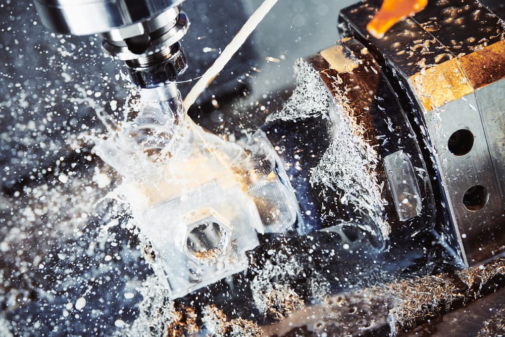 CNC milling machine cutting metal with coolant and fluid splashing across the workpiece — hazardous substances exposure