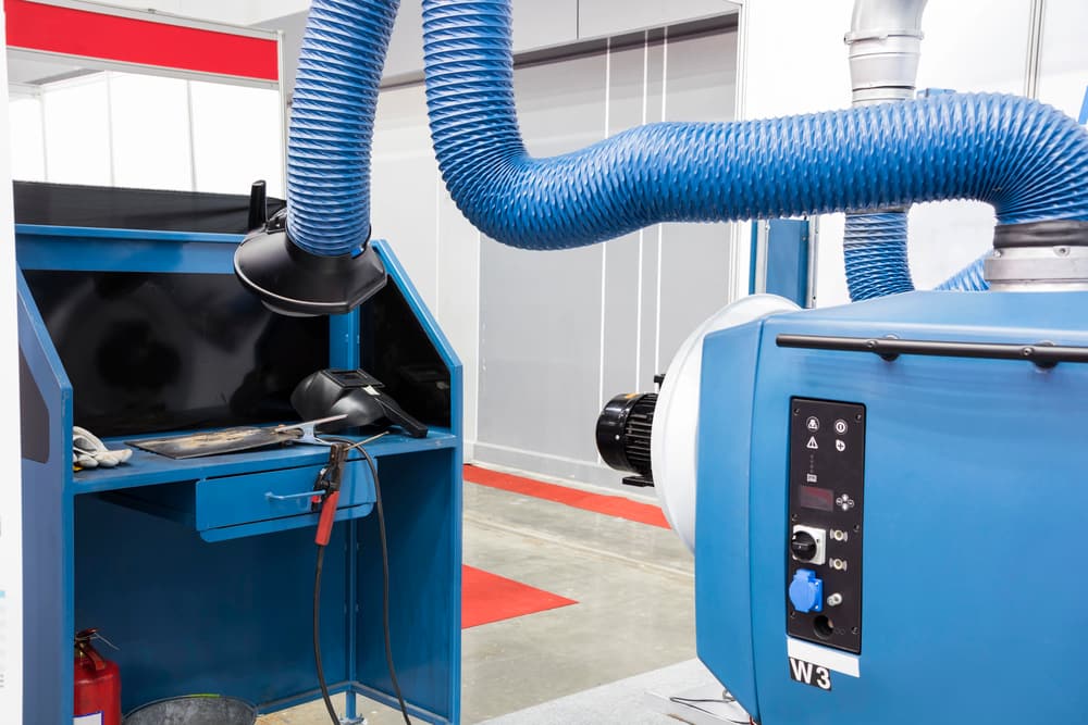 Welding bench fitted with on-tool extraction arms and a dust collector — local exhaust ventilation in use