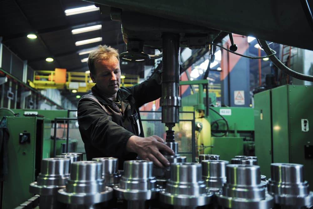 Operator working at a vertical metal press inside a manufacturing plant — rubber-process fume and dust environment