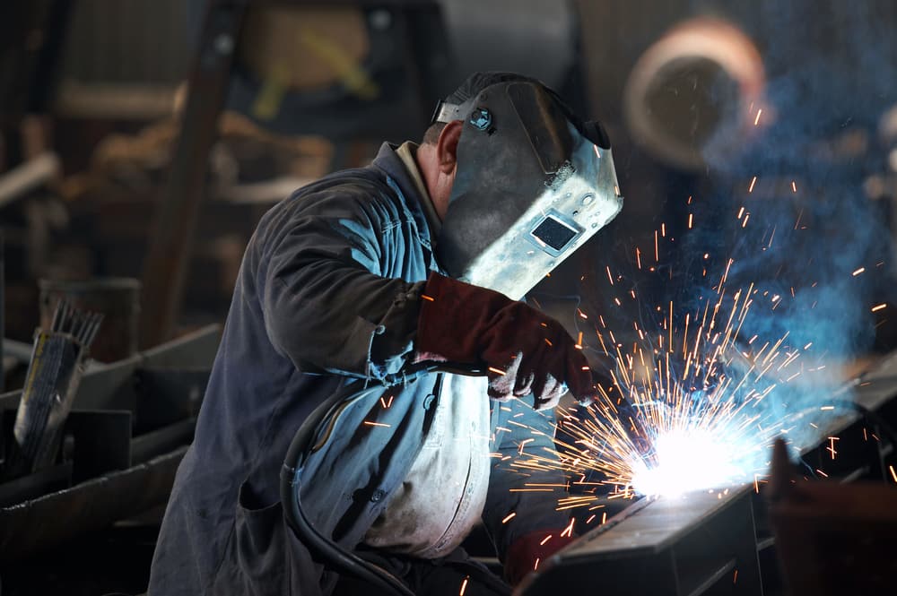 Welder in PPE striking an arc with bright sparks and a visible plume — welding fume exposure