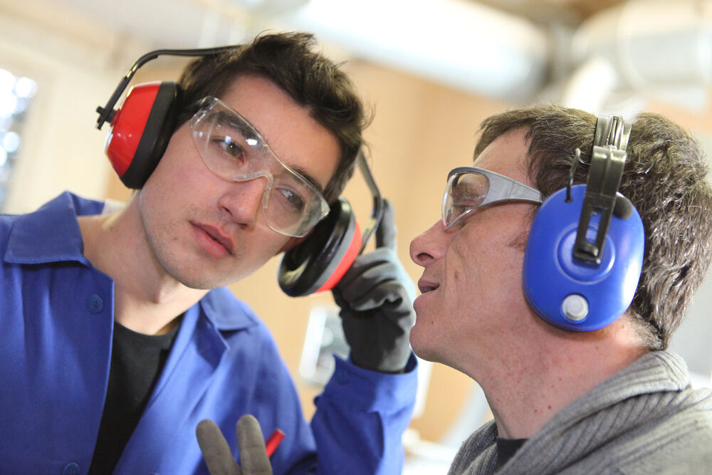 Two workers wearing ear defenders and safety glasses in a workshop